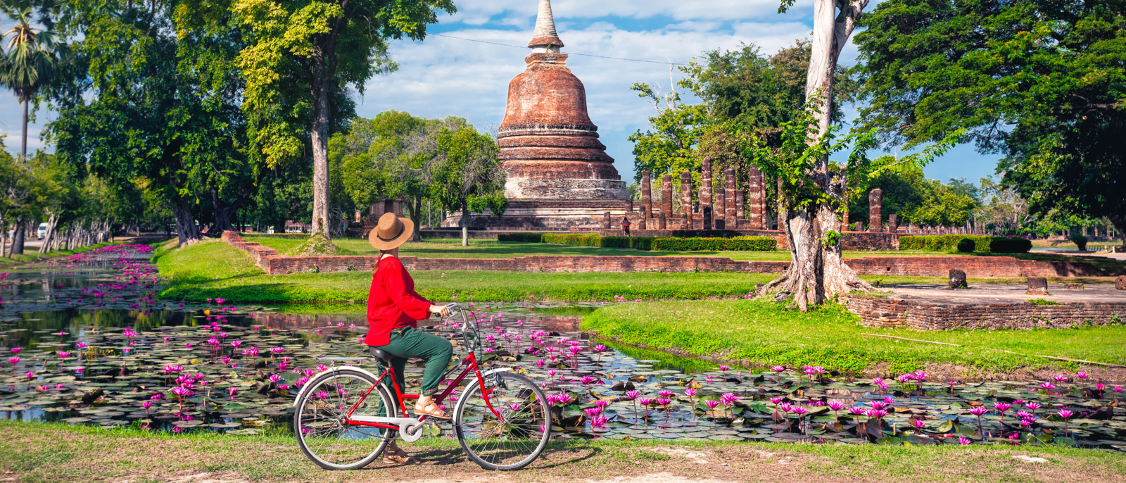 Femme en chemise rouge faisant du vélo en regardant le vieux temple bouddhiste du parc historique de Sukhothai, Thaïlande
