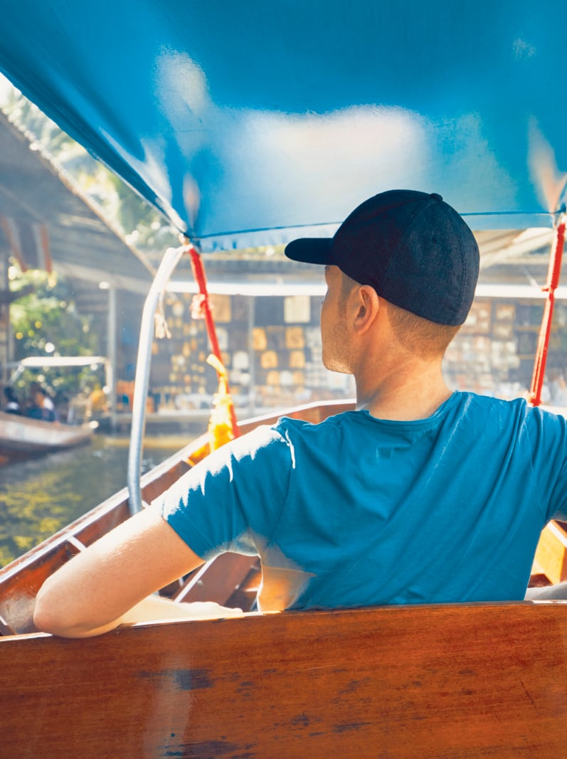 Young man (traveler) on the boat. Traditional floating market Damnoen Saduak in Ratchaburi near Bangkok, Thailand.