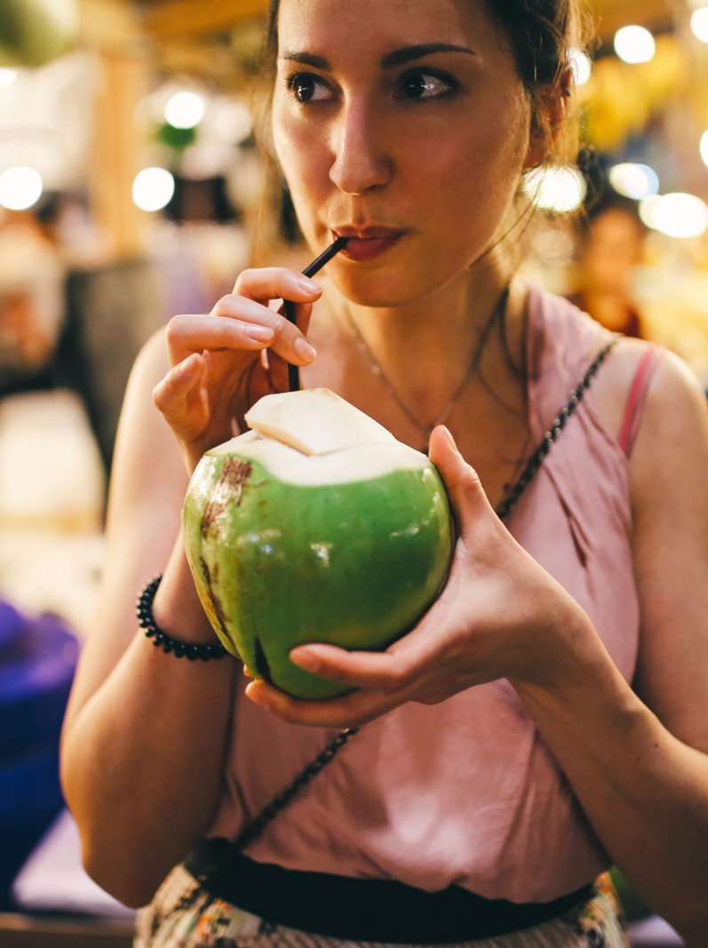Authentic Thai street food in Bangkok. Young woman is having a refreshment with delicious coconut water on a hot summertime evening.