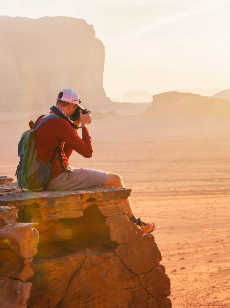 Tourist sits on edge of rock in Wadi Ram desert. Jordan sunset landscape
