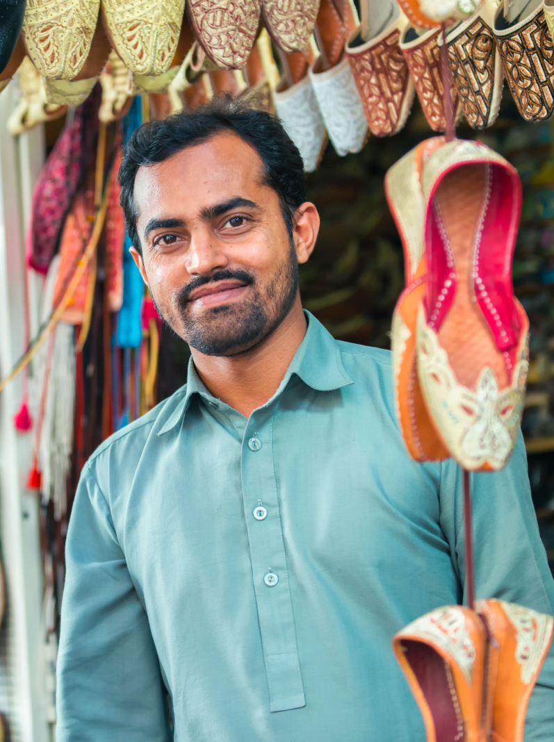 A friendly Indian vendor selling beautifully embroidered and beaded Middle Eastern women’s shoes from his stall at the Textile Souk in Bur Dubai near Dubai Creek