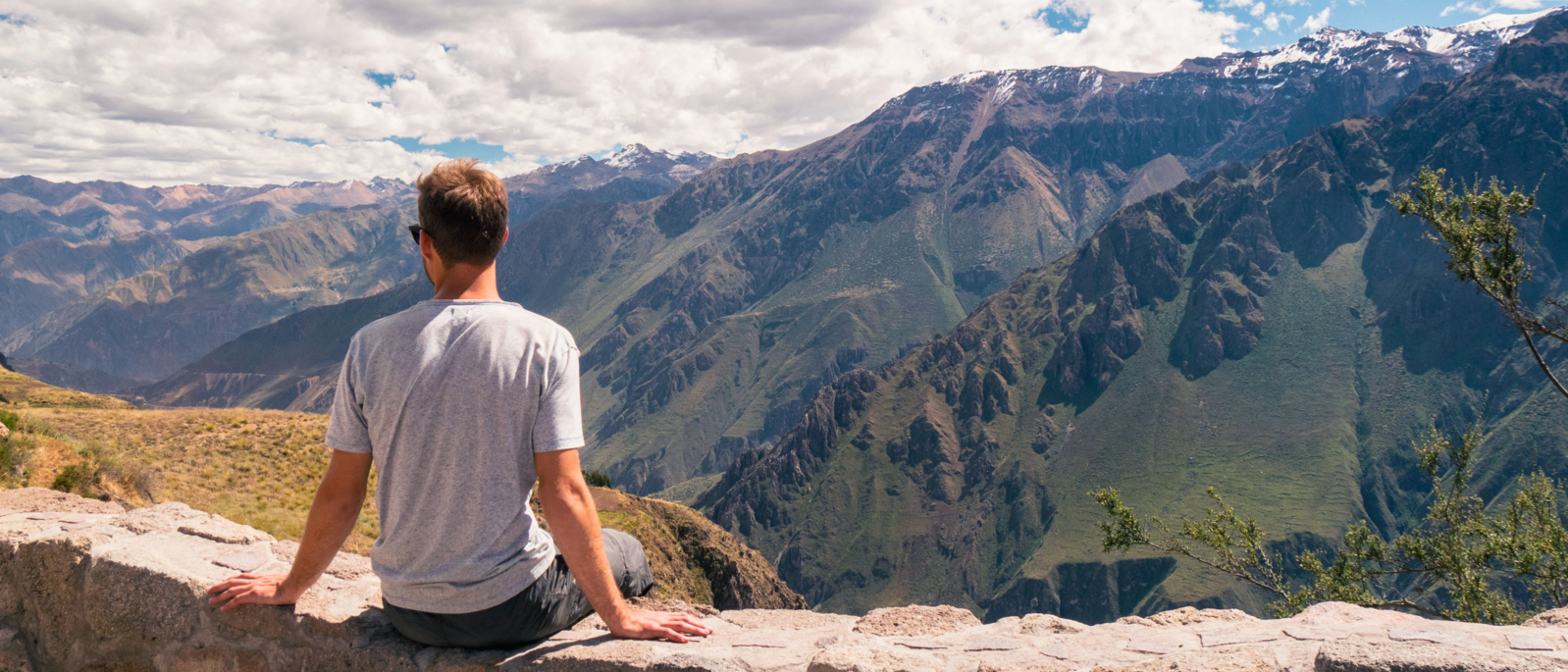 young white caucasian male man sitting enjoying landscape with colca canyon and surrounding mountains on a sunny day with few clouds in peru