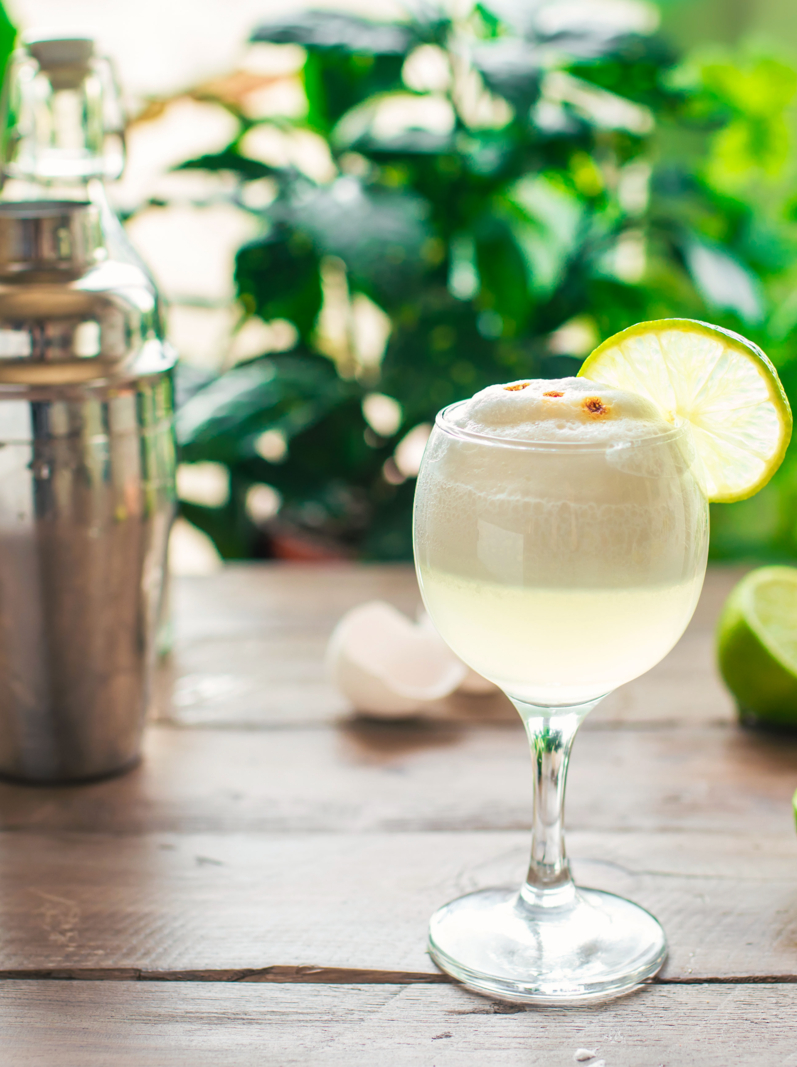 Pisco Sour Cocktail. Peruvian, Mexican, Chilean traditional drink pisco sour liqueur with lime and egg and bar equipment for making.