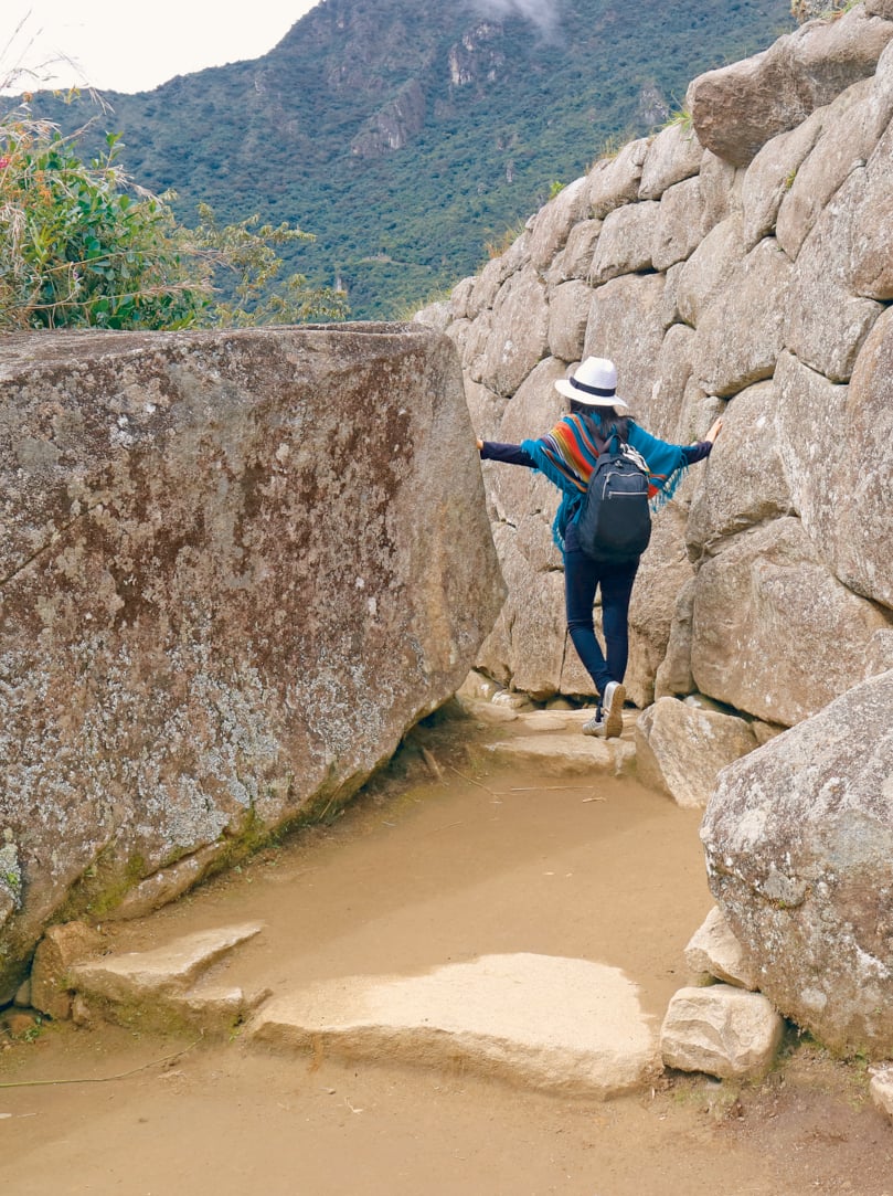 Female tourist exploring the ancient Inca ruins of Machu Picchu citadel in Cusco region, Archaeological site of Peru