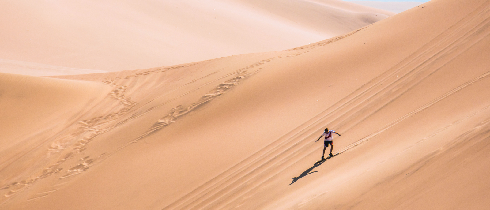 silhouette d'homme pratiquant le sandboard dans le désert du Pérou.