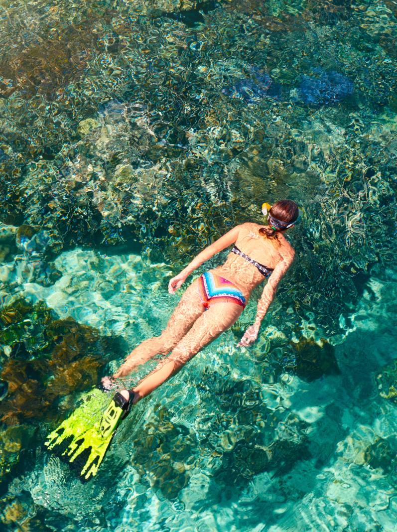 woman in swimsuit snorkeling in clear tropical sea above coral reef in sunny day. View from above