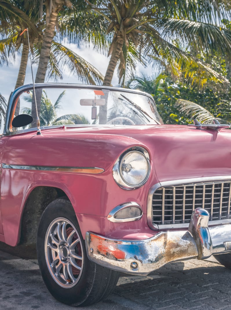 American pink classic car parked under palms near the beach in Cuba